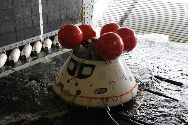 NASA image: Recovery team members work with a test version of Orion floating in the well deck of the U.S.S. Anchorage 