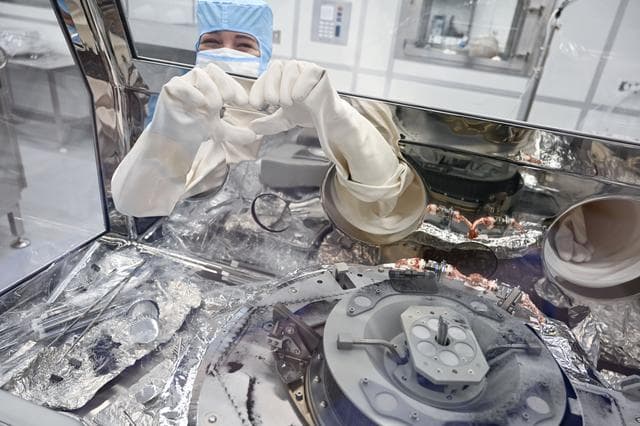 NASA image: jsc2024e011323 - Astromaterials processor Mari Montoya shows a hand heart while working in the OSIRIS-REx canister glovebox at NASA’s Johnson Space Center in Houston. Montoya was sweeping asteroid material on the avionics deck of the OSIRIS-REx canister