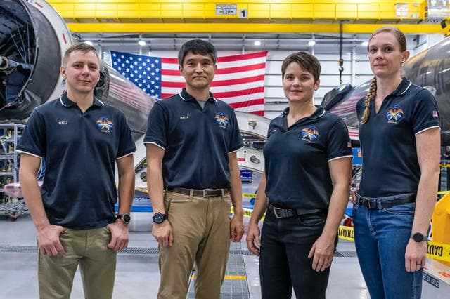 NASA image: SpaceX Crew-10 members stand in front of a Falcon 9 first-stage booster