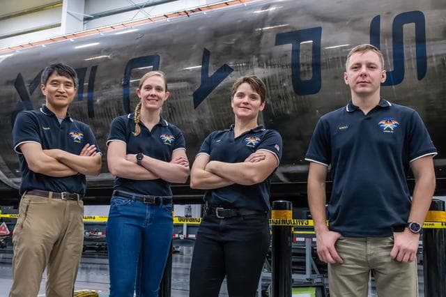 NASA image: SpaceX Crew-10 members stand in front of a Falcon 9 first-stage booster