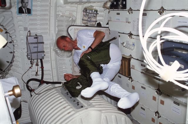 NASA image: Pilot Fullerton dons EES anti-gravity suit lower torso on middeck