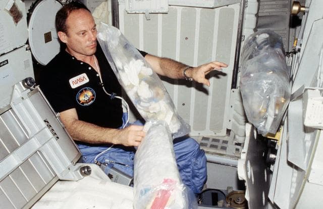 NASA image: Commander Lousma is surrounded by a week's worth of trash on the middeck