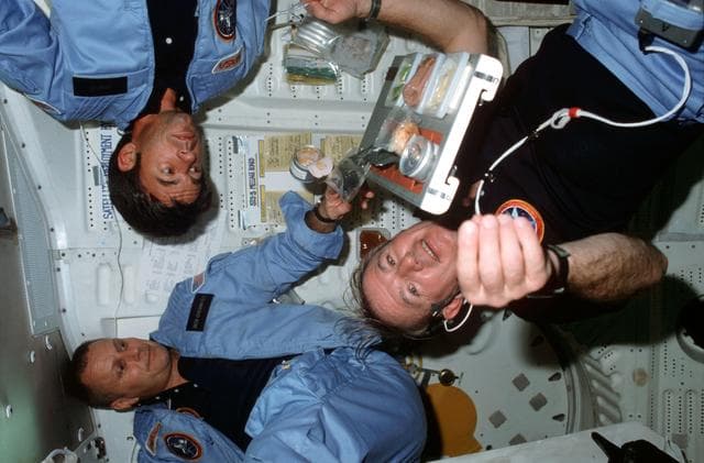 NASA image: STS-5 crewmembers with meal tray assembly on middeck