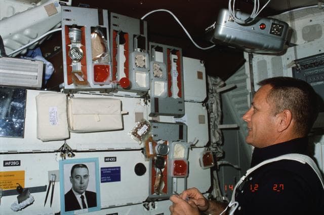 NASA image: Pilot Overmyer looks over food selections and experiments with beverage