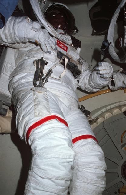 NASA image: Plastic toy shark drifts through airlock in front of EMU suited MS Lenoir