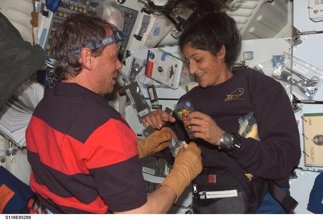 NASA image: STS-116 crewmembers Williams and Fuglesang prepare to open food packages on the MDDK on Space Shuttle Discovery