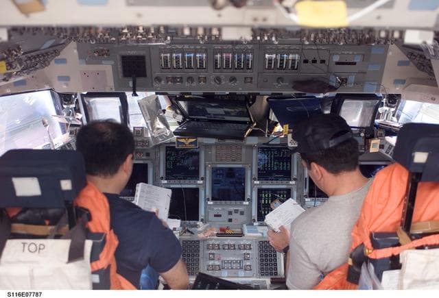 NASA image: STS-116 Crewmembers Polansky and Oefelein look over crew procedures in the FWD FD on Space Shuttle Discovery