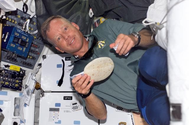 NASA image: Lindsey holds a tortilla he is preparing on the MDK during STS-121
