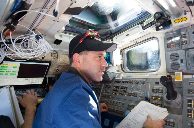 NASA image:   STS-125 Crew working on the Shuttle Atlantis Flight Deck during HST Rendezvous/Berthing