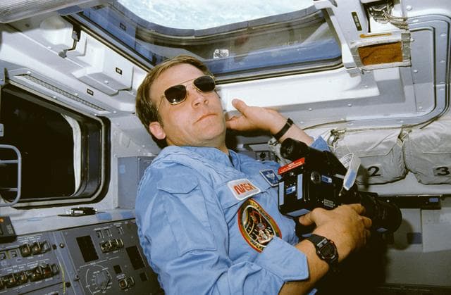NASA image: STS-30 MS Lee, wearing sunglasses, uses 70mm camera on aft flight deck