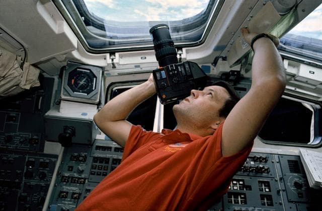 NASA image: STS-41 Pilot Cabana points ROLLEI camera out aft flight deck overhead window