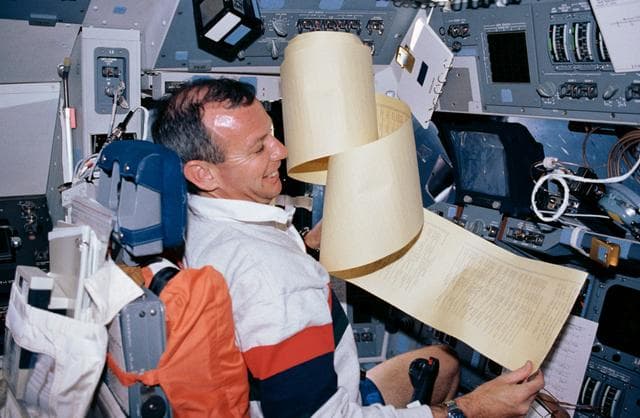 NASA image: STS-45 Pilot Duffy wrestles with a TAGS printout on OV-104's flight deck