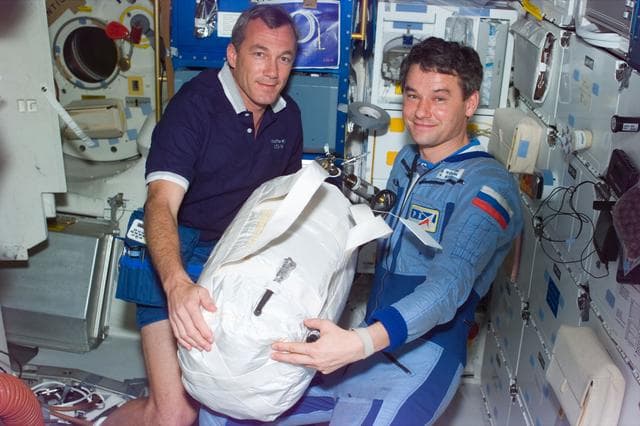 NASA image: Astronaut Wilcutt hands water transfer bag to Mir 22 commander on middeck
