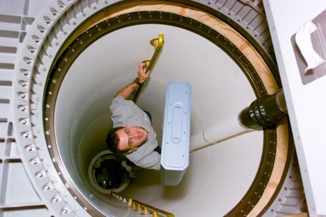 NASA image: MS Wisoff moves stowage item through transfer tunnel