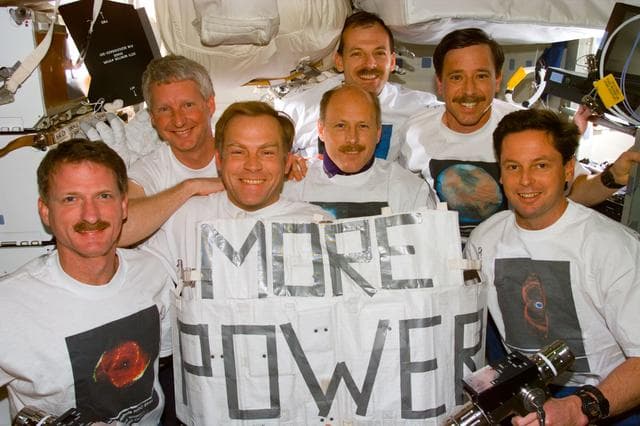 STS-82 crew portrait with "More Power" banner and Hubble shirts