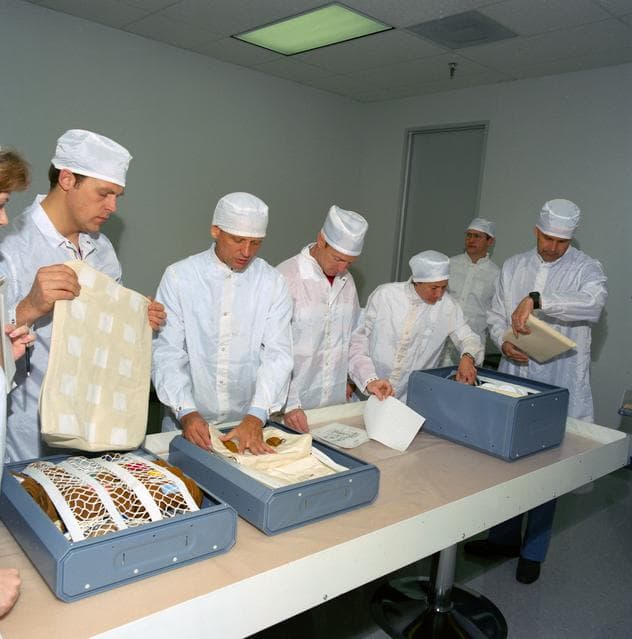 NASA image: STS-30 clean-suited crewmembers examine locker contents during bench review