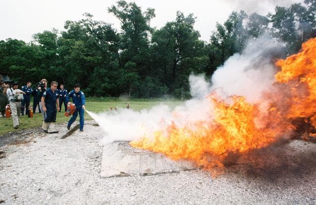 NASA image: STS-41 crewmembers use fire extinguishers to control blaze at JSC's fire pit