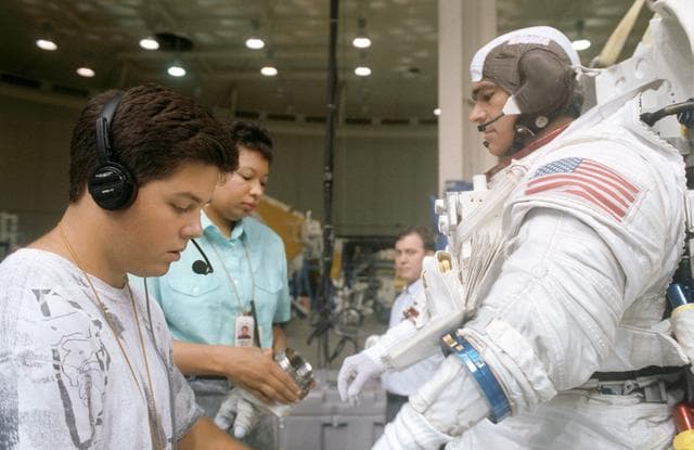 NASA image: STS-53 MS Clifford, in EMU, dons gloves with technicians' assistance at JSC