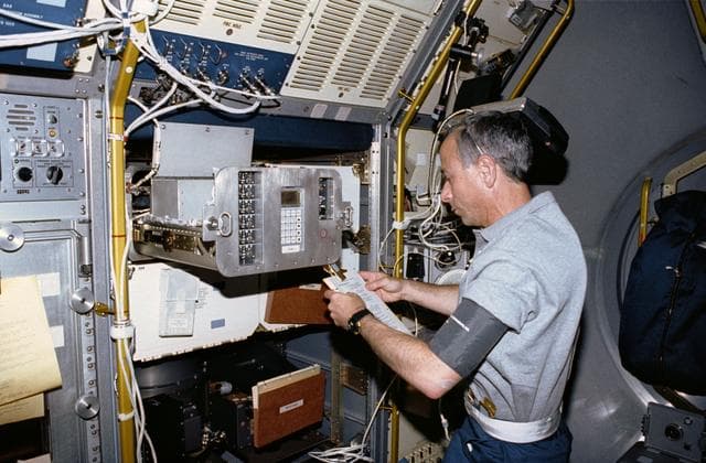 NASA image: Crewmember working on the spacelab Generic Bioprocessing Apparatus, rack #10.