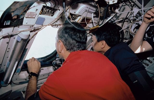 NASA image: Two male crewmembers in the aft flight deck, looking out the windows.