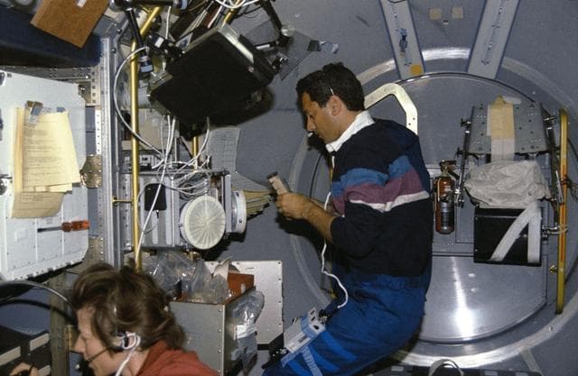 NASA image: Crewmembers in the spacelab with Generic Bioprocessing Apparatus, Rack #10.
