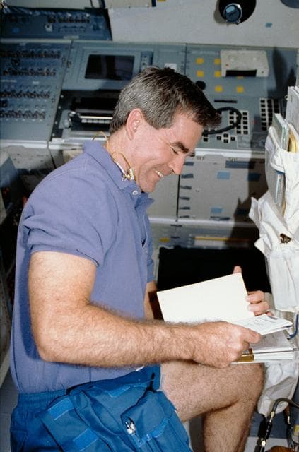 NASA image: Crewmember in the aft flight deck reviewing a procedures manual.