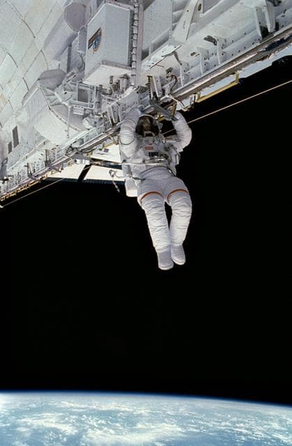 NASA image: EVA Crewmember in the payload bay crawling along the starboard rail.