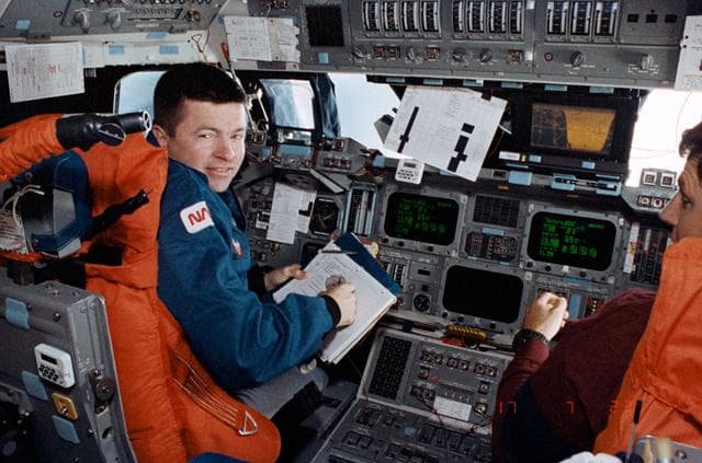 NASA image: Crewmembers in the fwd flight deck reviewing inflight procedures manual.