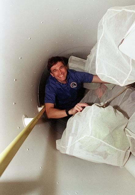 NASA image: Astronauts move through narrow space in tunnel adapter filled with transfer bag