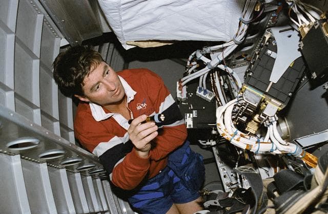 NASA image: Henricks examines the computer systems under the Spacelab floor