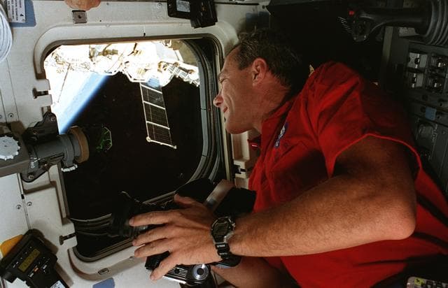 NASA image: STS-79 crew at aft flight deck overhead windows with Mir in background