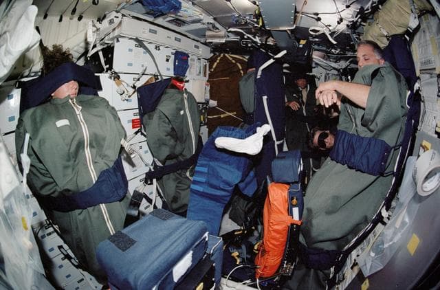 NASA image: STS-112 crew in their sleep restraints on the orbiter middeck